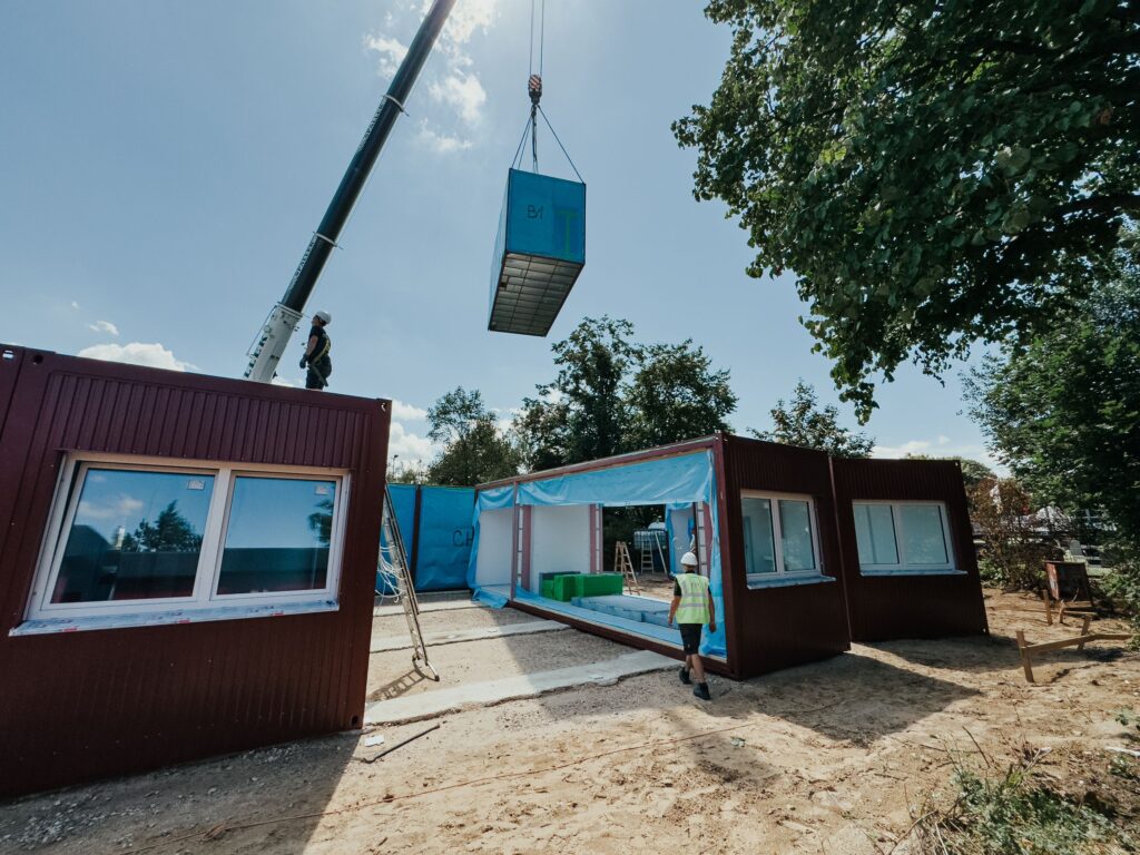 Baustart in Rheine: Schule nimmt Form an 5 Aufnahme vom Bauprojekt in Rheine, wo rote Sanitärcontainer mit einem Kran angeliefert werden