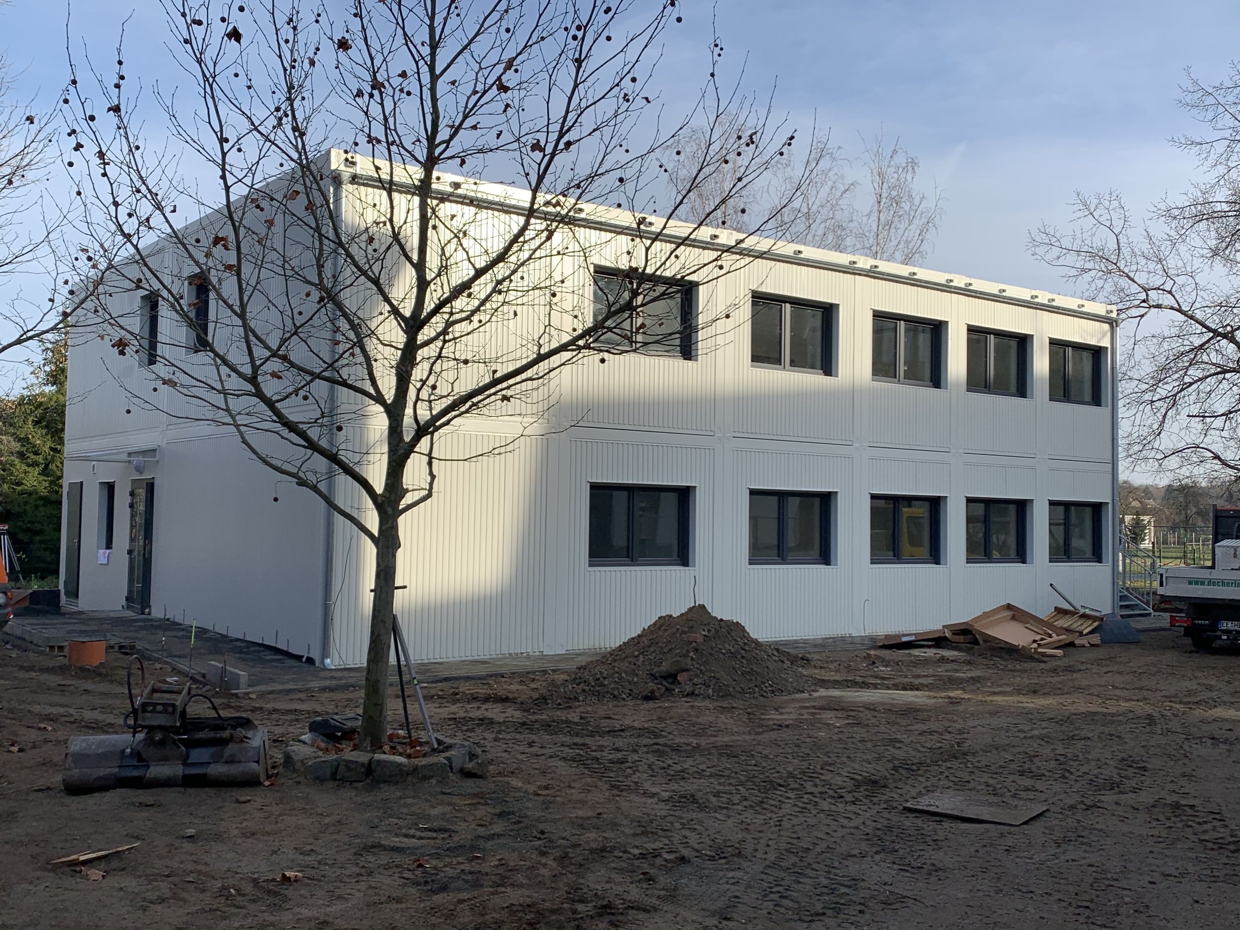 Aufnahme der im Bau befindlichen Hort in Modulbauweise, zu sehen ein zweistöckiges Gebäude mit einem Baum und Baugeräten davor