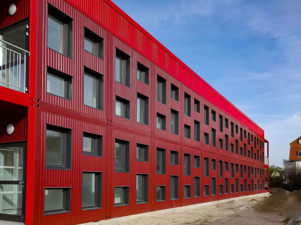 Fertigstellung einer 2-geschossigen Schule in Modulbauweise in Helmstedt 1 Ansicht der roten Grundschule in Modulbauweise in Helmstedt mit zwei Etagen und grauen Fenstern