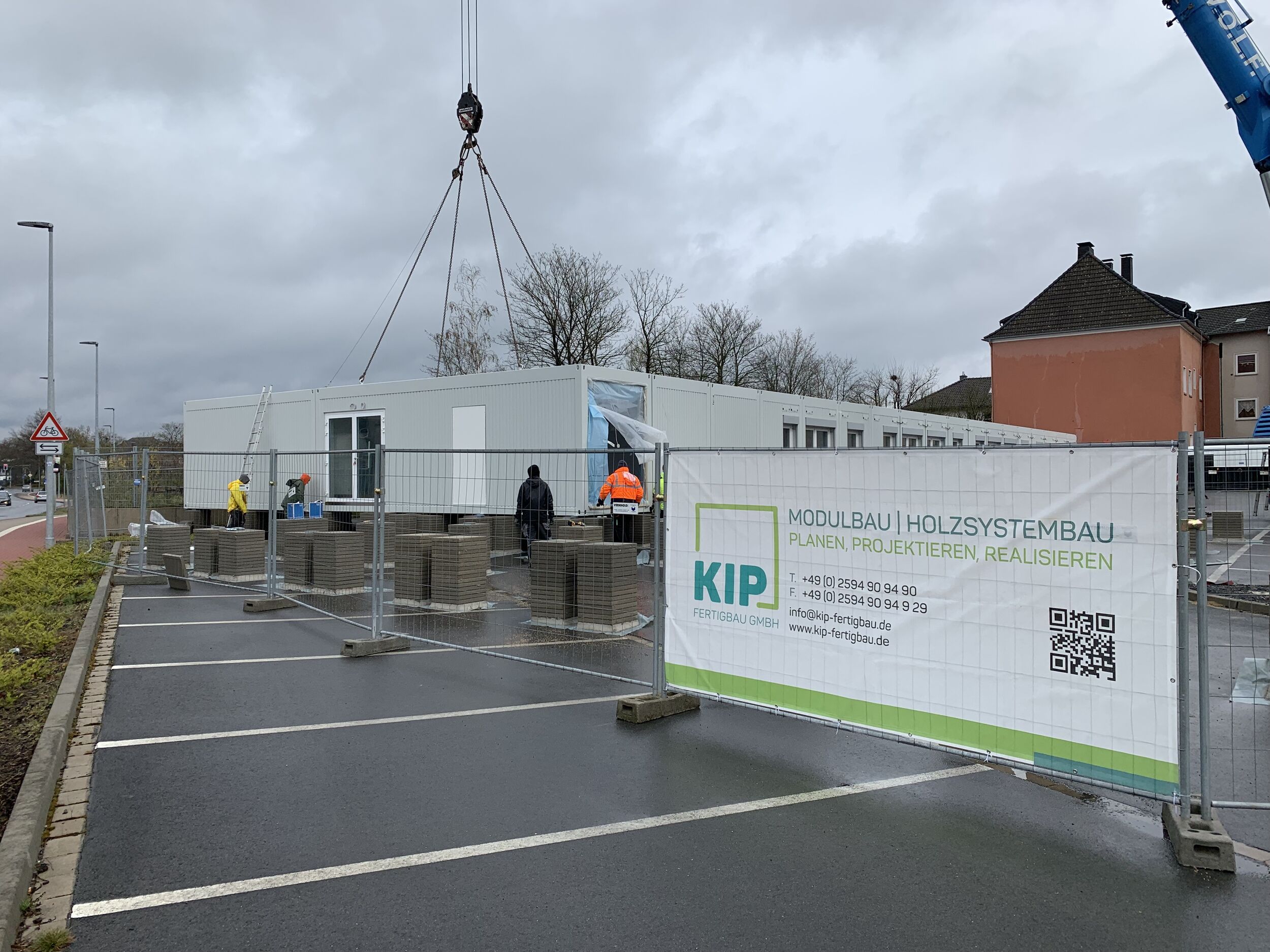 Aufnahme der Baustelle der Interimsschule in Dorsten mit einem Bauzaun im Vordergrund, sowie einem Container am Haken eines Mobilkrans