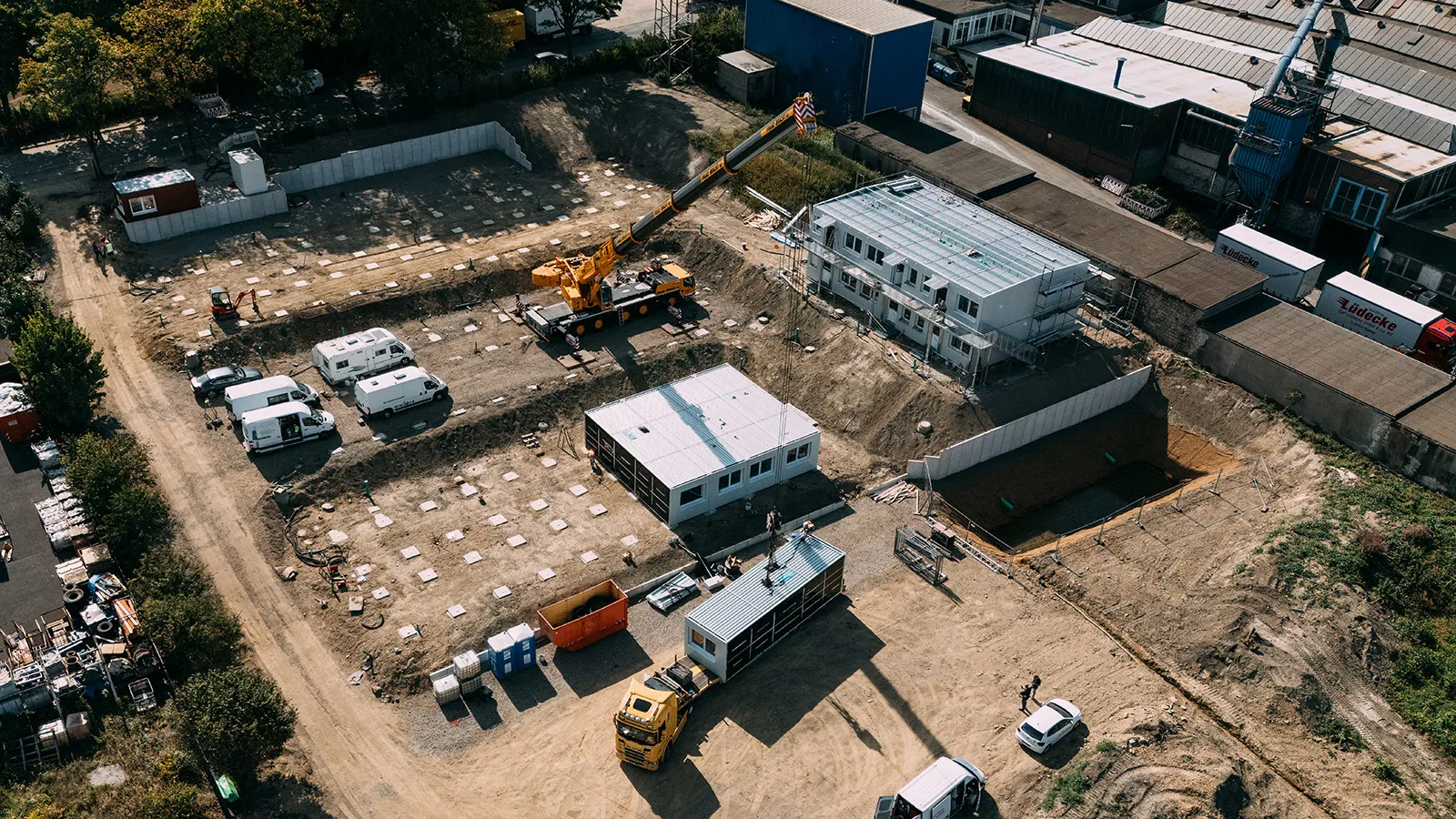 Aufsicht mittels Drohne auf die Baustelle der Wohnanlage in Velbert, ein Kran hebt Containermodule von einem Tieflader